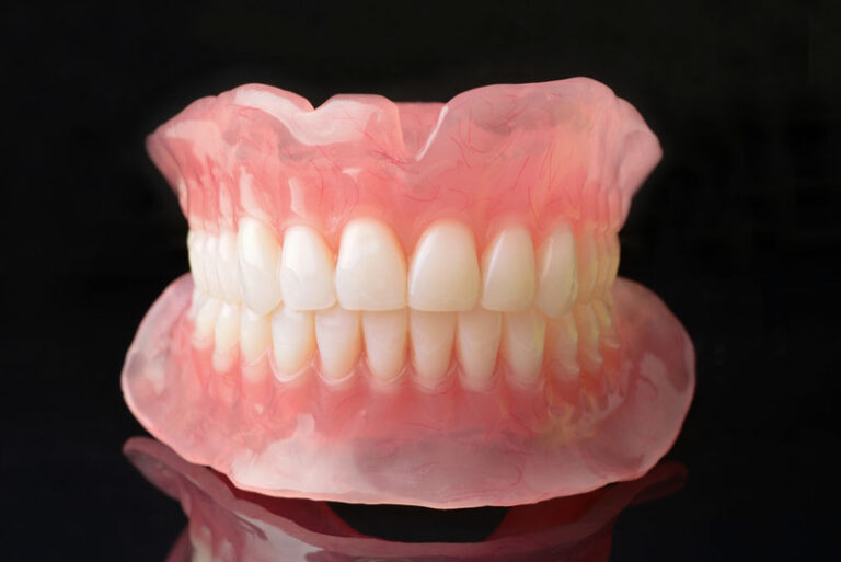 Full set of upper and lower complete dentures with natural-looking teeth and pink acrylic base displayed on a black background.