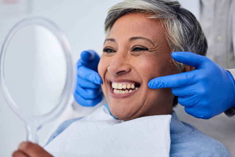 Smiling dental patient holding a mirror while dentist points at her teeth after successful dental treatment.