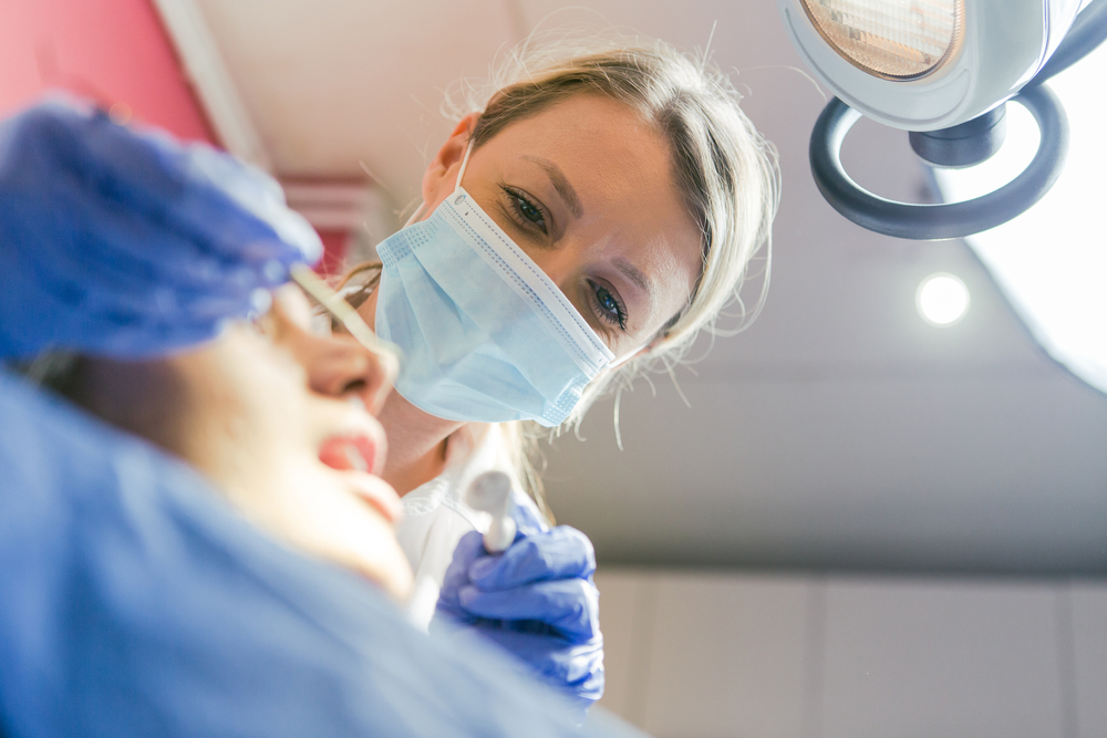 Image of a dentist consulting with a patient, pointing to a 3D scan of the patient's jaw with dental implants placed. No text on image.